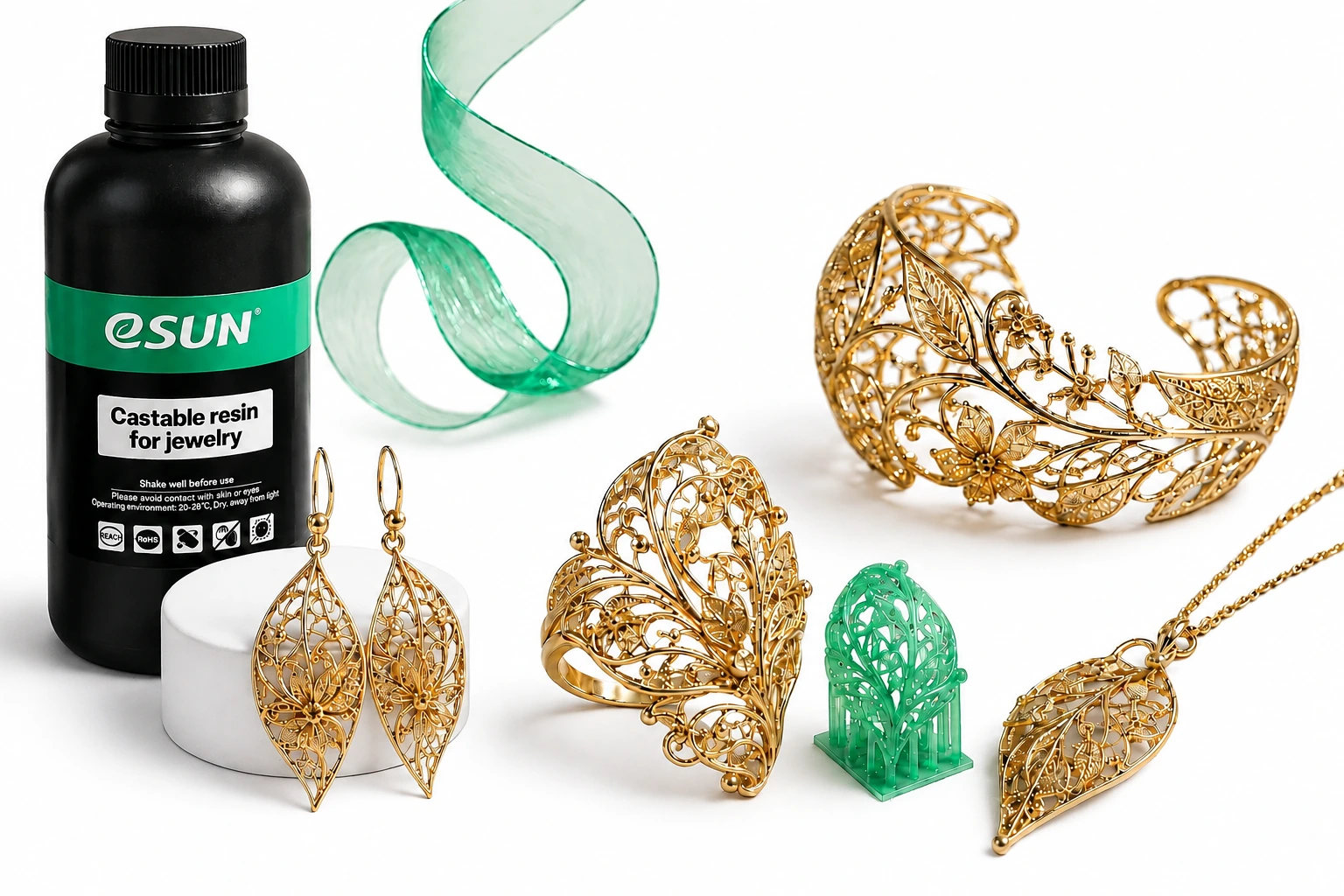 Composition artistique de bijoux dorés sur fond blanc, avec modèle en résine verte, ruban émeraude et grand flacon eSUN Jewellery Green